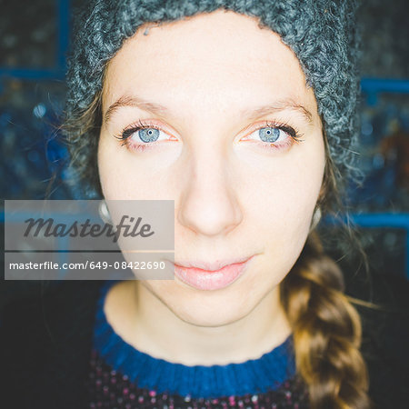 Close up portrait of young woman with plaited hair wearing knit hat looking at camera smiling