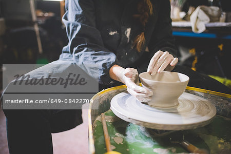 Young woman sitting at pottery wheel making clay pot