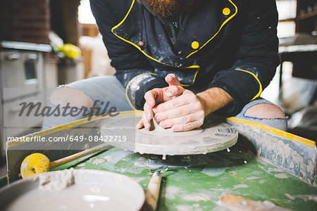 Cropped front view of mid adult man shaping clay on pottery wheel