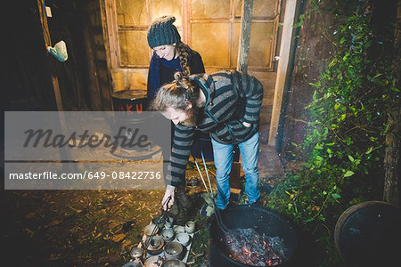 Couple using tongs to remove clay pots from fire, smiling