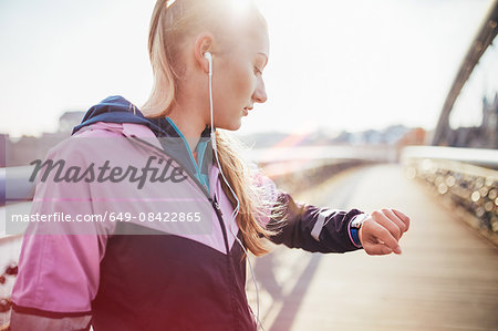 Mid adult female runner checking time on footbridge Mid adult female runner checking time on footbridge