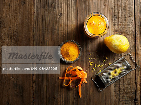 Overhead view of yellow raw juice with grated lemon and carrot on wood grain pattern background