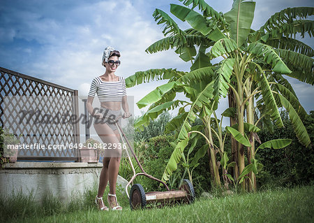 Young stylish woman pushing lawnmower in garden