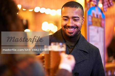 Couple on night out, holding beer glasses making a toast smiling