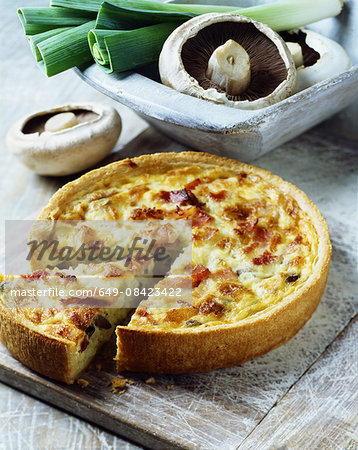 Ham, mushroom and leek quiche on white washed chopping board