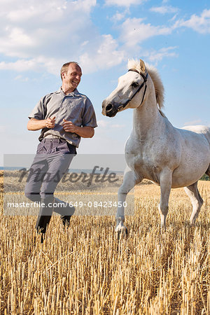 Male trainer running in front of white horse in field