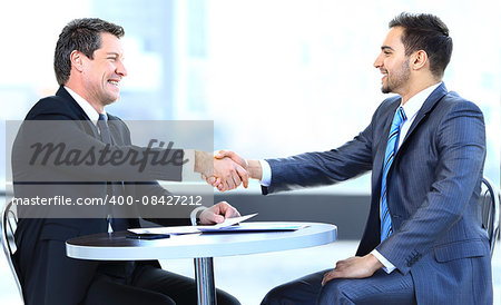 Business colleagues sitting at a table during a meeting with two male executives shaking hands
