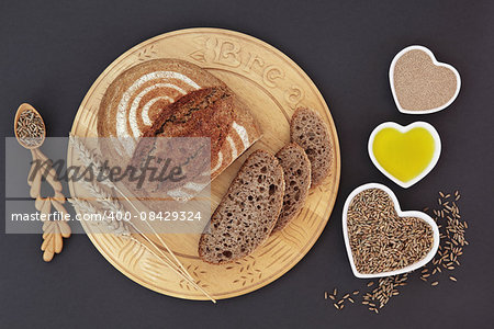 Rustic homemade rye bread on wooden board with wheat sheaths, yeast, olive oil and rye grain in heart shaped dishes and spoon.