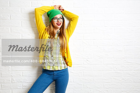 Smiling Hipster Girl at White Brick Wall Background. Street Syle. Trendy Casual Fashion Outfit in Spring or Autumn. Copy Space.