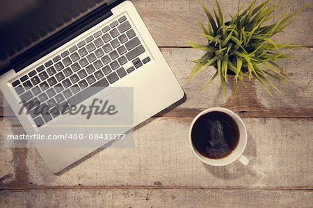 Work desk with laptop computer, plant pot and hot coffee cup. Top view rustic wooden table background with copy space in vintage toned.