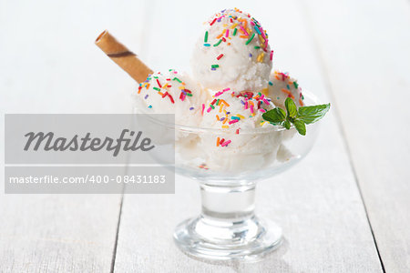 Scoop coconut ice cream in cup with waffle on white wooden background.