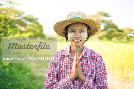 Portrait of a young Burmese female farmer with thanaka powdered face in blessing gesture.