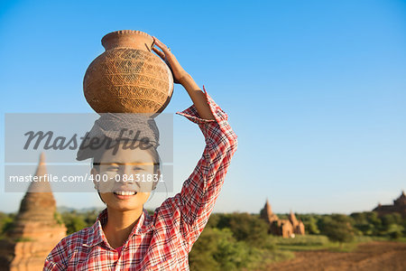 Portrait of Young Asian Burmese traditional female farmer carrying clay pot on head, Bagan, Myanmar