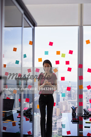 Mixed race secretary working in modern office in skyscraper, writing and sticking adhesive notes with tasks on window.