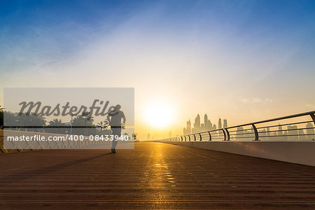 jogger on an empty boardwalk running against the sun with the skyline of Dubai in the background, UAE, Middle East