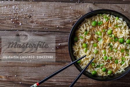 Top view of chinese noodles with fresh peas and chopped green onion on wooden table.