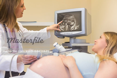 Doctor scanning pregnant patients belly and showing the fetus at the ultrasound clinic