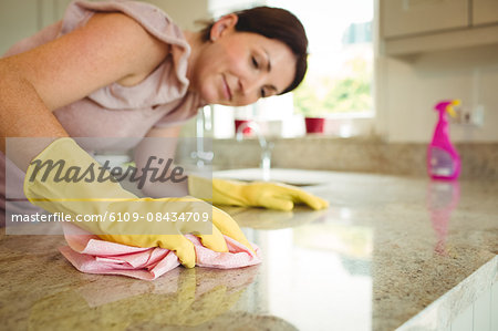 Woman cleaning kitchen counter with cloth in rubber gloves