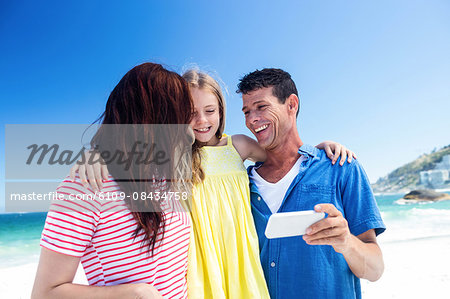 Cute family looking at smartphone on the beach