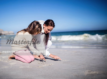 Mother and son drawing in the sand on the beach