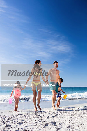 Cute family holding hands and walking on the beach