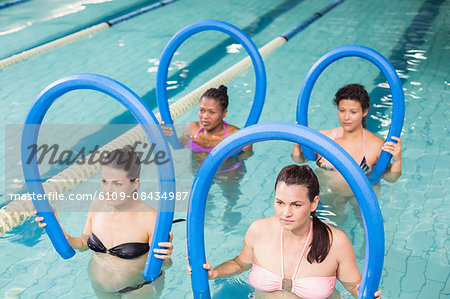 Pregnant women exercising with foam rollers at the swimming pool