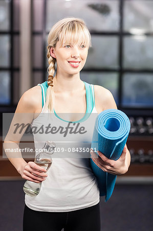 Smiling woman holding exercise mat and water bottle at the leisure center