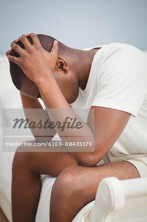 Man with headache holding his head sitting on his bed