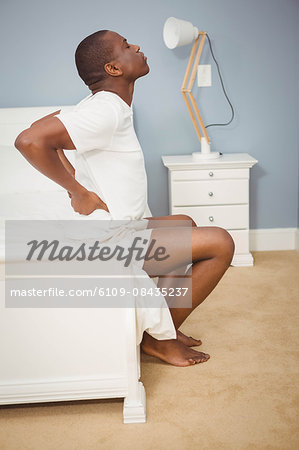 Man having back pain sitting on his bed