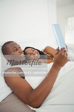 Ethnic couple using tablet in the bed