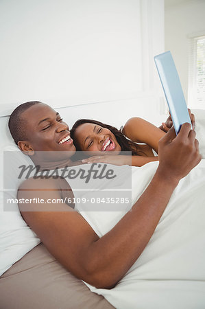 Ethnic couple using tablet in the bed