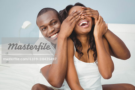 Man covering his girlfriend eyes in the bedroom