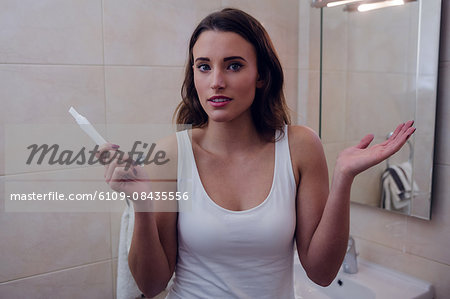 Doubtful beautiful brunette gesturing with a pregnancy test in the bathroom at home