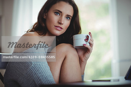 Thoughtful beautiful brunette using tablet while drinking coffee in the living room at home