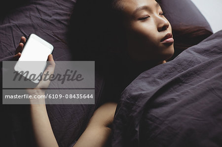 Brunette sleeping on the bed with smartphone at home