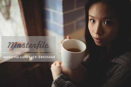 Brunette drinking tea sitting on the kitchen counter at home
