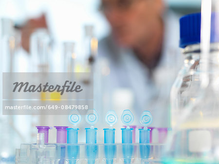 Row of eppendorf vial awaiting sample for testing in laboratory, scientist out of focus in background Row of eppendorf vial awaiting sample for testing in laboratory, scientist out of focus in background