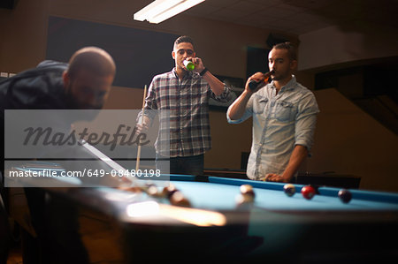 Man playing pool, friends drinking beer in background