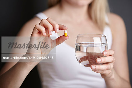 Cropped shot of young woman holding medicine capsule and glass of water