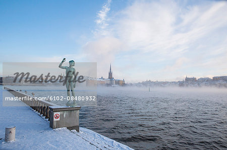 Statue, city at sea on background