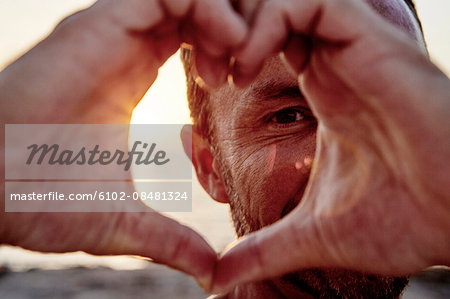 Portrait of man making heart-shape on beach