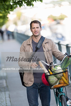 Portrait of man holding bicycle with vegetables in basket