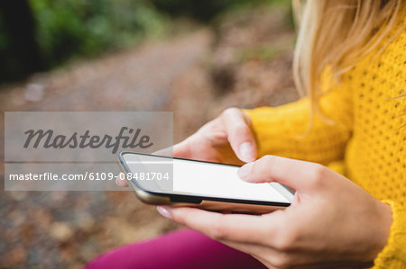 Beautiful blonde woman using smartphone in the woods