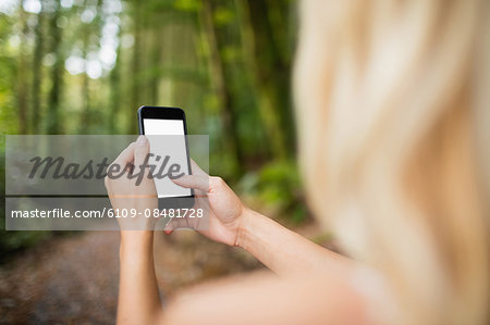 Beautiful blonde woman using smartphone in the woods