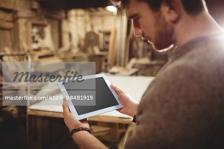 Happy carpenter using his tablet in a dusty workshop