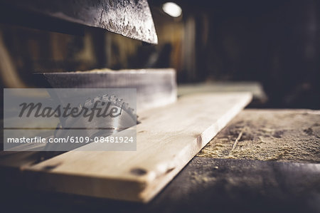 Saw sawing plank of wood in a dusty workshop