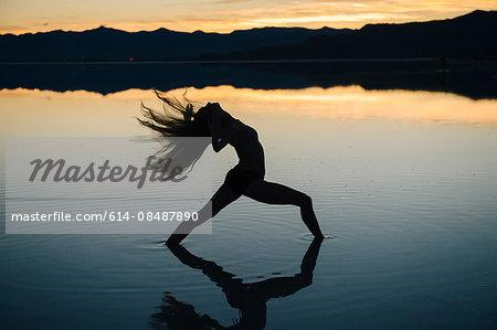 Silhouetted female dancer throwing back her long hair in lake at sunset, Bonneville Salt Flats, Utah, USA
