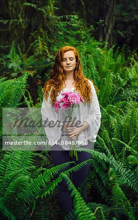 Young woman holding bunch of pink gerberas amongst forest ferns