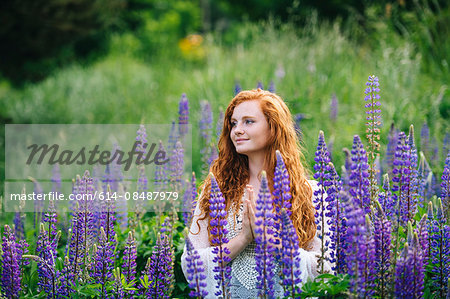 Serene young woman meditating with hands together amongst purple wildflowers