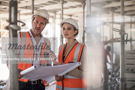 Female and male builders with blueprint on construction site